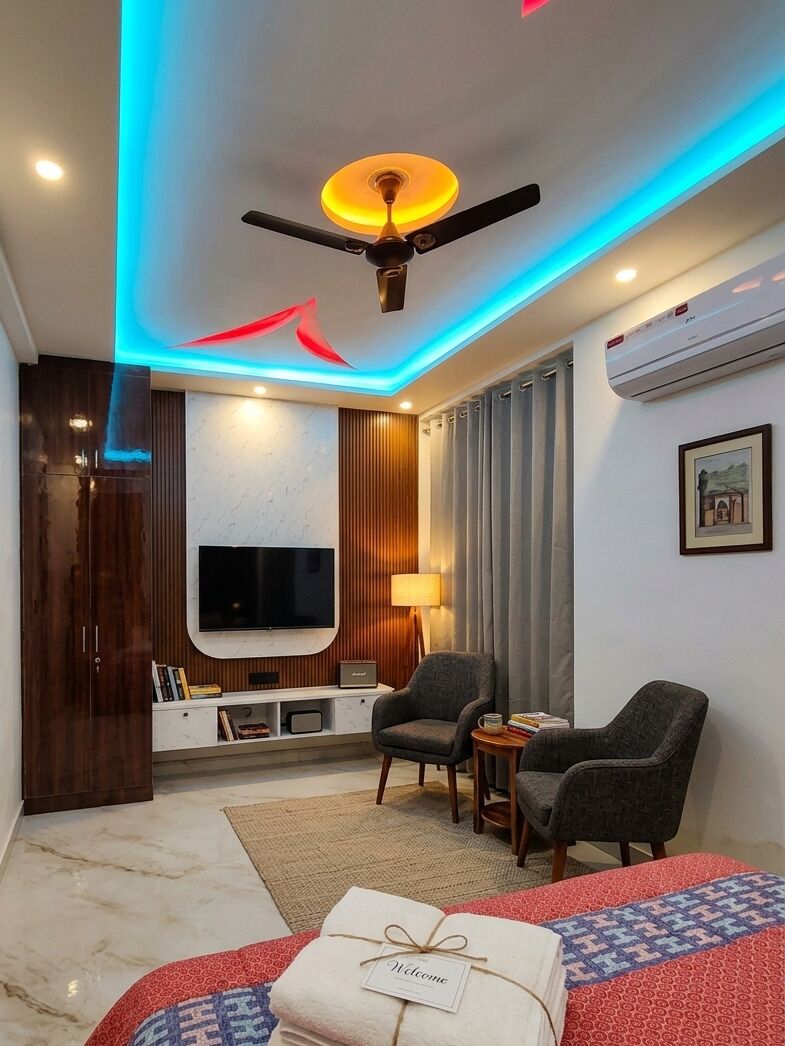 Een moderne hotelkamer met een plafondventilator, een flatscreen-tv, een zithoek met twee stoelen, een kleine tafel en een bed met een rood- en blauw geborduurde spreidekker.