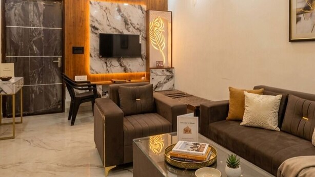 Uma sala de estar moderna com sofá, mesa de centro, TV fixada numa parede de mármore e iluminação circular no teto.