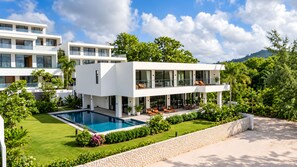 Ein modernes, zweistöckiges Haus mit Swimmingpool, Sitzgelegenheiten im Freien und üppiger Bepflanzung.