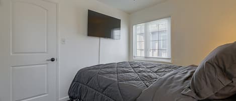Un dormitorio con cama, ventilador de techo, televisor montado y ventana con persianas.