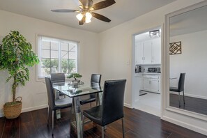 A dining area with a glass table, black chairs, a ceiling fan, and a view into a kitchen.