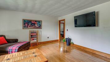 A living room with a wooden coffee table, a couch, a painting, a television, and a potted plant.