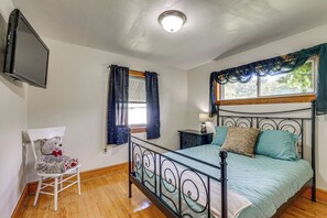 A bedroom with a metal bed frame, a bedside table with a lamp, a chair with a teddy bear, and a TV mounted on the wall. - Quiet Stuart Retreat w/ Yard & Fireplace (Stuart)