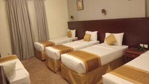 Quarto de hotel com quatro camas de solteiro, cabeceira de madeira, escrivaninha e uma cadeira.