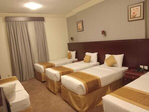 Habitació d'hotel amb quatre llits individuals, un panell de fusta al capçal, un escriptori i una cadira.