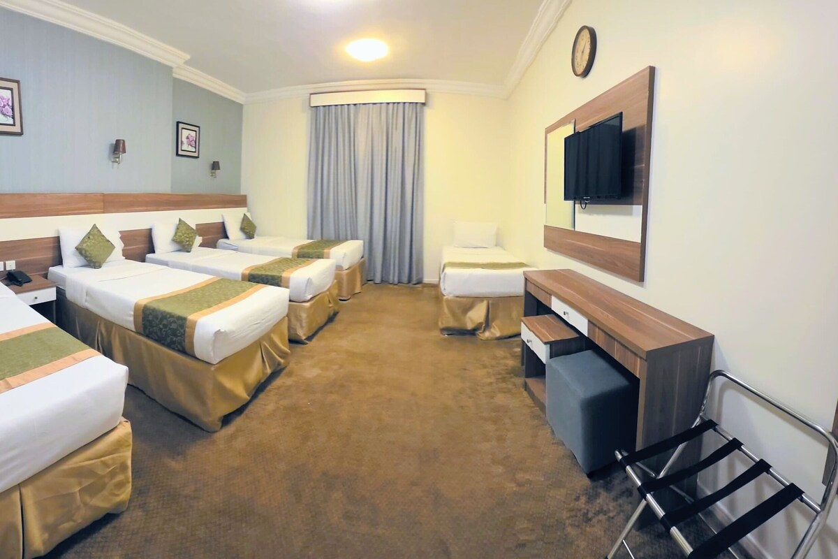 A hotel room with four beds, a desk, a chair, a mirror, a clock, and a window with curtains.