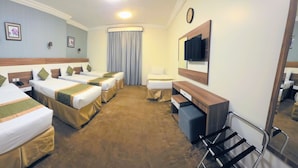 A hotel room with four beds, a desk, a chair, a mirror, a clock, and a window with curtains. - sama hijaz almaqam Hotel (Mecca)