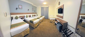A hotel room with four beds, a desk, a chair, a mirror, a clock, and a window with curtains. - sama hijaz almaqam Hotel (Mecca)