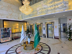 A lobby with a chandelier, flags, a vending machine, and a reception desk. - sama hijaz almaqam Hotel (Makkah)
