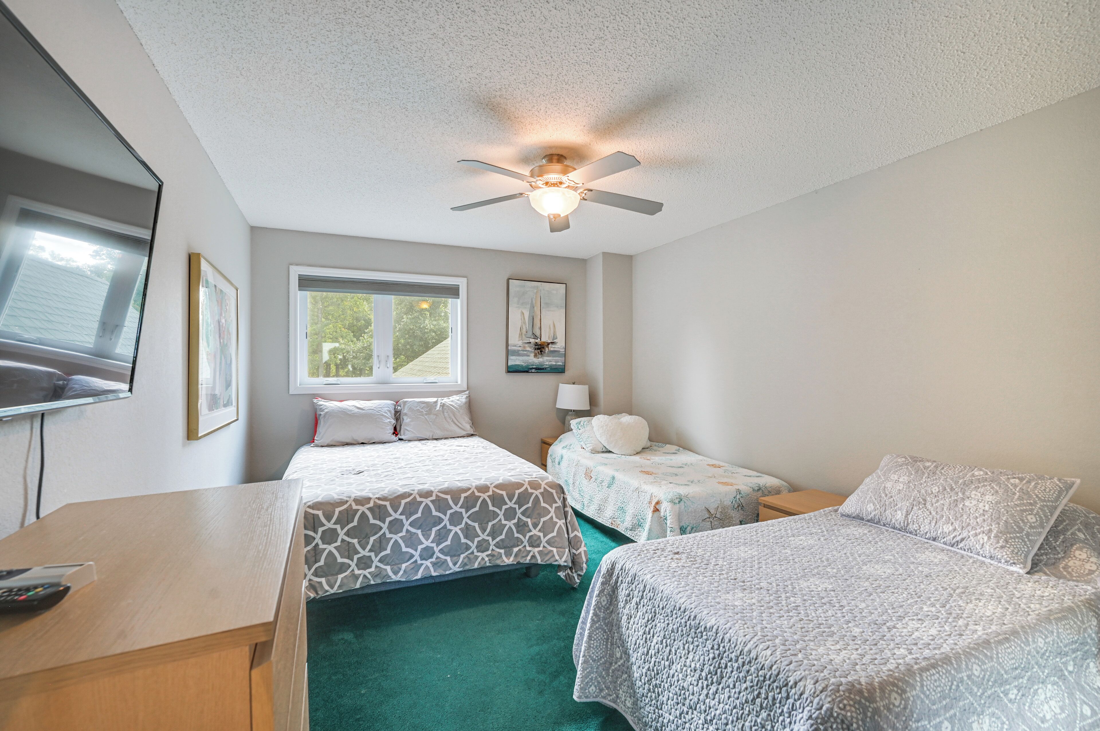 A room with two beds, a ceiling fan, a window, and a TV.