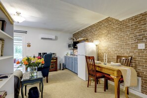 A compact kitchen with a dining area, a brick wall, and a window. - Easy Raleigh Access! Quaint Apt w/ Patio (Garner)