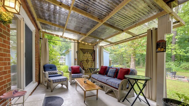 A covered patio with wicker furniture, a wooden table, and a view of the garden. - Easy Raleigh Access! Quaint Apt w/ Patio (Garner)
