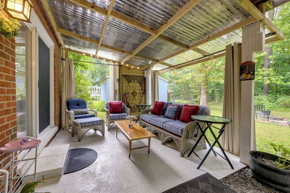 A covered patio with wicker furniture, a wooden table, and a view of the garden. - Easy Raleigh Access! Quaint Apt w/ Patio (Garner)