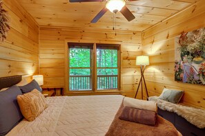 A wooden cabin room with a bed, a standing lamp, and a painting. - Private Hot Tub & Deck! Cherry Log Gem (Cherry Log)