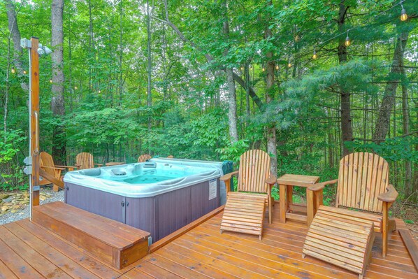 A hot tub surrounded by wooden deck chairs and a wooden table, set in a forested area. - Private Hot Tub & Deck! Cherry Log Gem (Cherry Log)