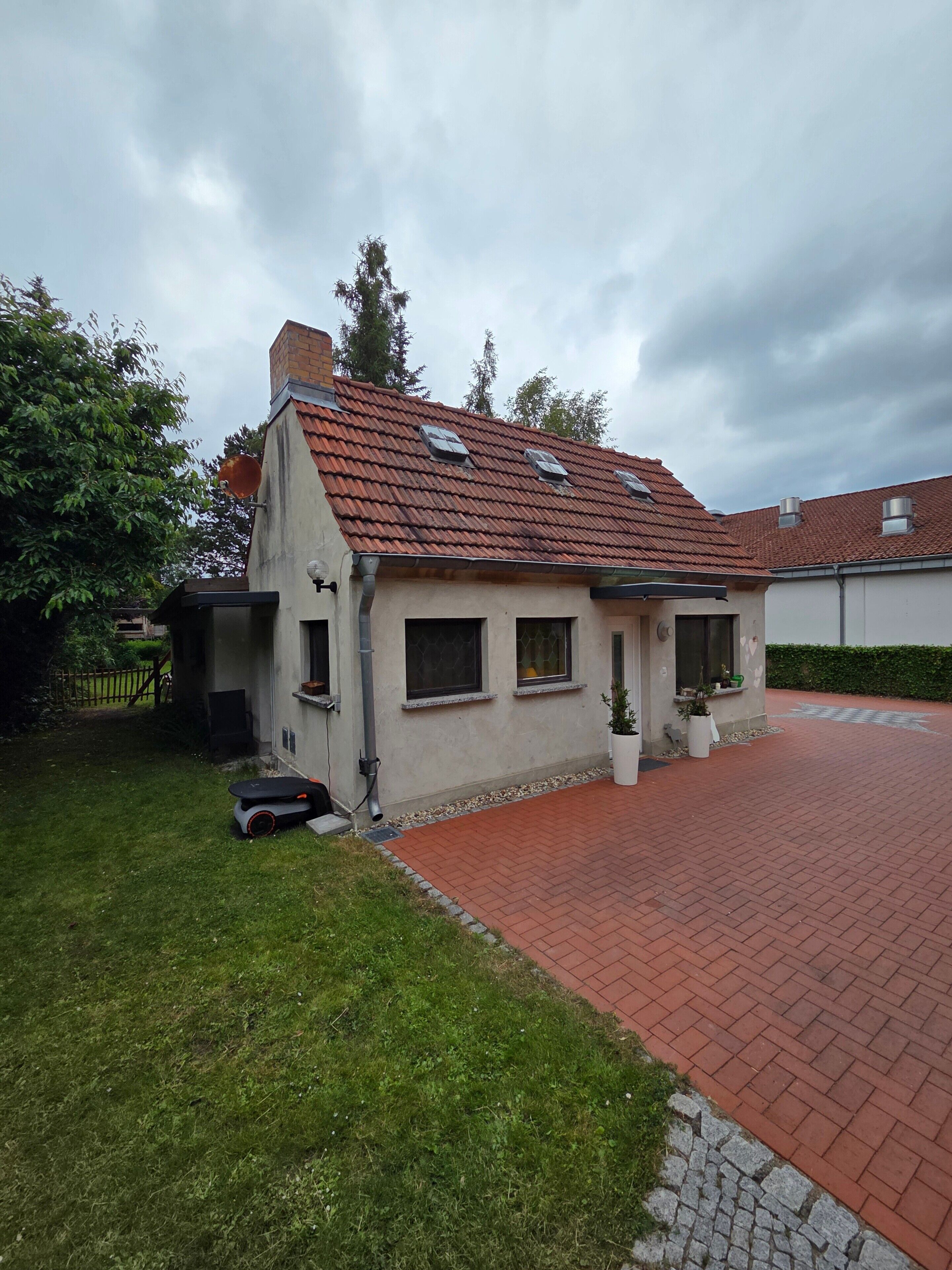 Ein kleines, eingeschossiges Haus mit rotem Ziegeldach, einem gepflasterten Einfahrt und einem gepflegten Rasen.