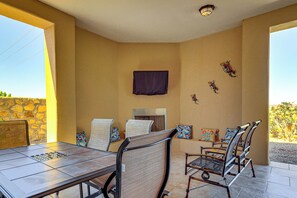 An outdoor dining area with a table and chairs, a stone wall, and a view of the landscape. - Las Cruces Oasis: Patio, Hot Tub + Mtn Views (Las Cruces)