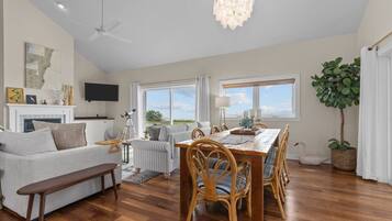 A spacious living room with a dining area, wooden flooring, and large windows offering a view.