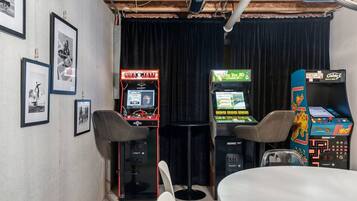 A room with arcade games, a table, and framed pictures on the wall.