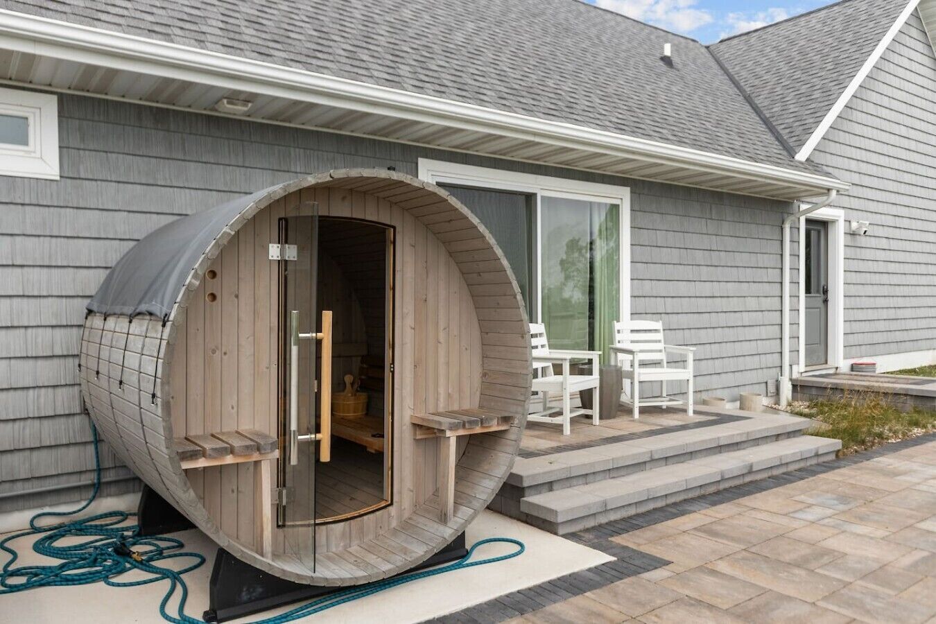 A sauna with a wooden exterior, a sliding glass door, and a small outdoor seating area with chairs.