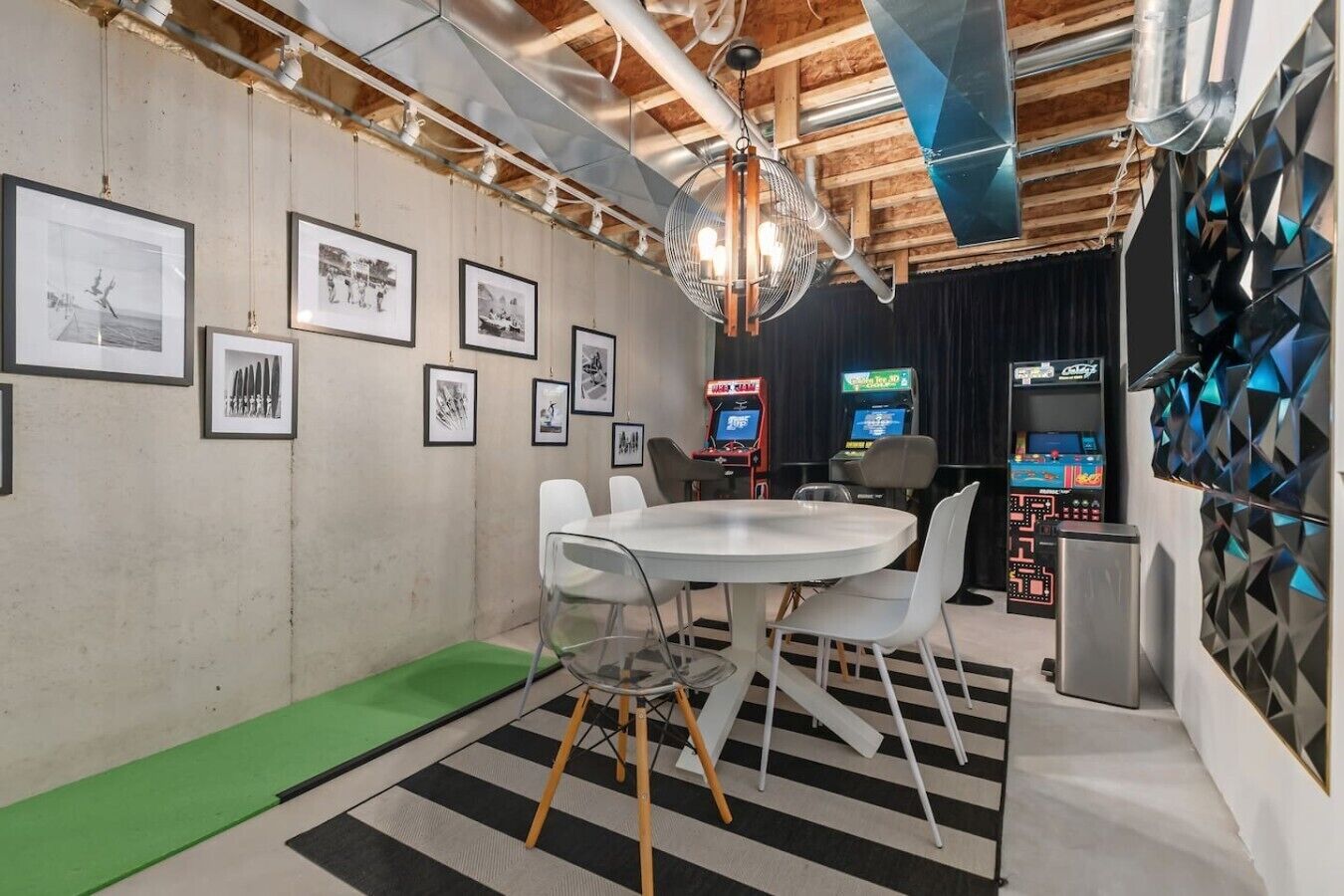 Un espace de bureau moderne avec une table ronde, des chaises, des tableaux encadrés au mur et des bornes d’arcade rétro.