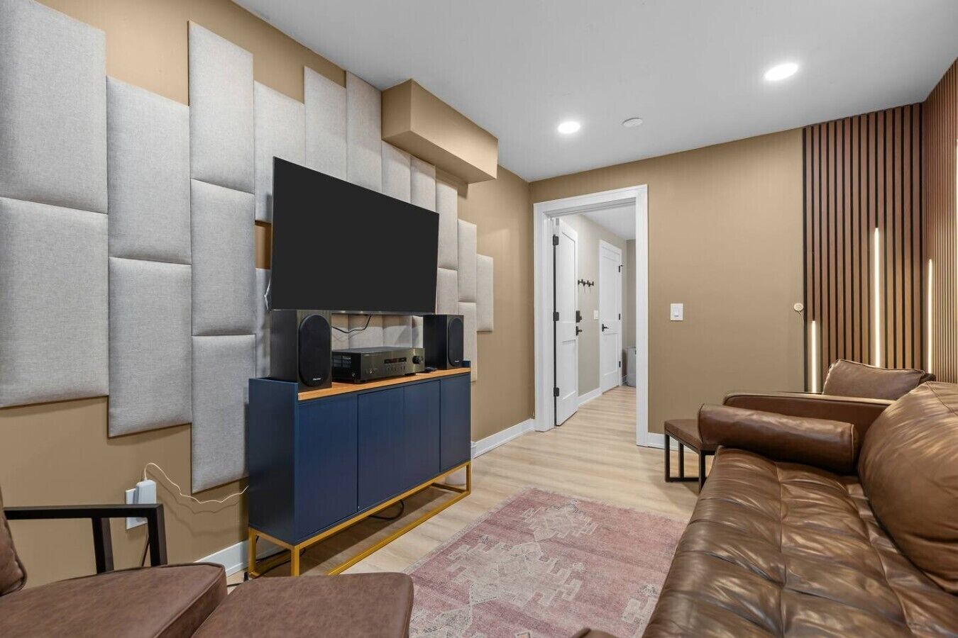 A modern living room with a flat-screen TV, a blue entertainment unit, a brown leather sofa, and a patterned rug.
