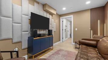 A modern living room with a flat-screen TV, a blue entertainment unit, a brown leather sofa, and a patterned rug.