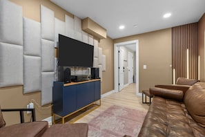 A modern living room with a flat-screen TV, a blue entertainment unit, a brown leather sofa, and a patterned rug.