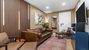 Una sala de estar moderna con un sofá de cuero marrón, sillones a juego, una mesa de centro, un televisor y un espejo grande.