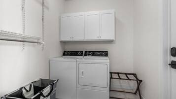 Un lavadero con lavadora y secadora de carga frontal, un tendedero y un cubo de basura.
