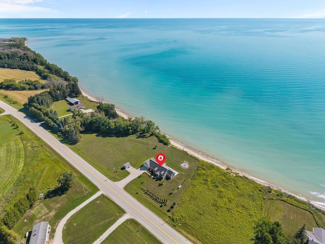 An aerial view of a coastal property with a large body of water, a road, and a building with a red marker.