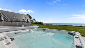 Ett bubbelbad med utsikt över havet, omgivet av en gräsyta och en överbyggd konstruktion.