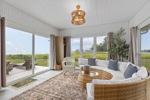 A spacious room with a large window, a white sofa set, a wicker coffee table, and a hanging light fixture.