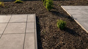A landscaped outdoor area with a paved walkway, a tree, and a grassy field.
