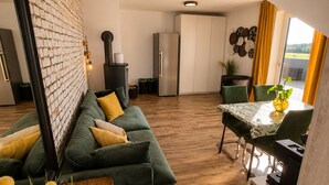 A modern kitchen with a brick wall, a dining area with a table and chairs, and a green sofa with yellow cushions.