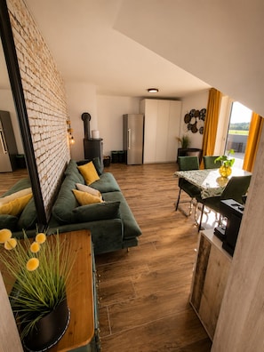 A modern kitchen with a brick wall, a dining area with a table and chairs, and a green sofa with yellow cushions.