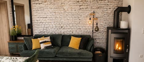 A cozy living room with a green sofa, a fireplace, and a brick wall.