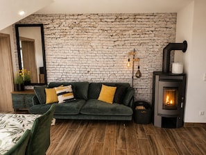 A cozy living room with a green sofa, a fireplace, and a brick wall.