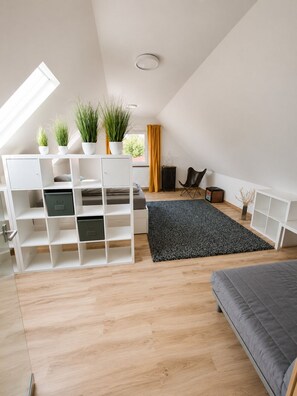 A modern loft bedroom with a skylight, built-in storage, a grey sofa, and a black rug.