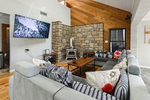 Uma sala de estar moderna com uma parede de pedra, lareira, TV de tela plana grande e sofá seccional cinza.