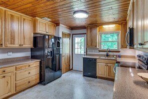 A kitchen with wooden cabinets, a stainless steel refrigerator, a dishwasher, and a window with a view of greenery. - Mary Esther Family Home, 9 Mi to Navarre Beach! (Mary Esther)