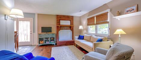 A living room with a fireplace, a sofa, a TV, and a window with blinds.