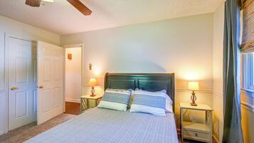 A bedroom with a bed, two bedside tables, a ceiling fan, and a window with curtains.
