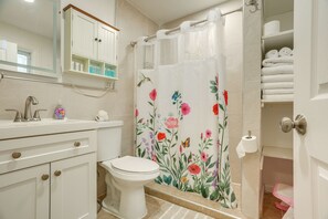 Et badeværelse med toilet, vask, spejl og bruseforhæng med blomstermotiv.