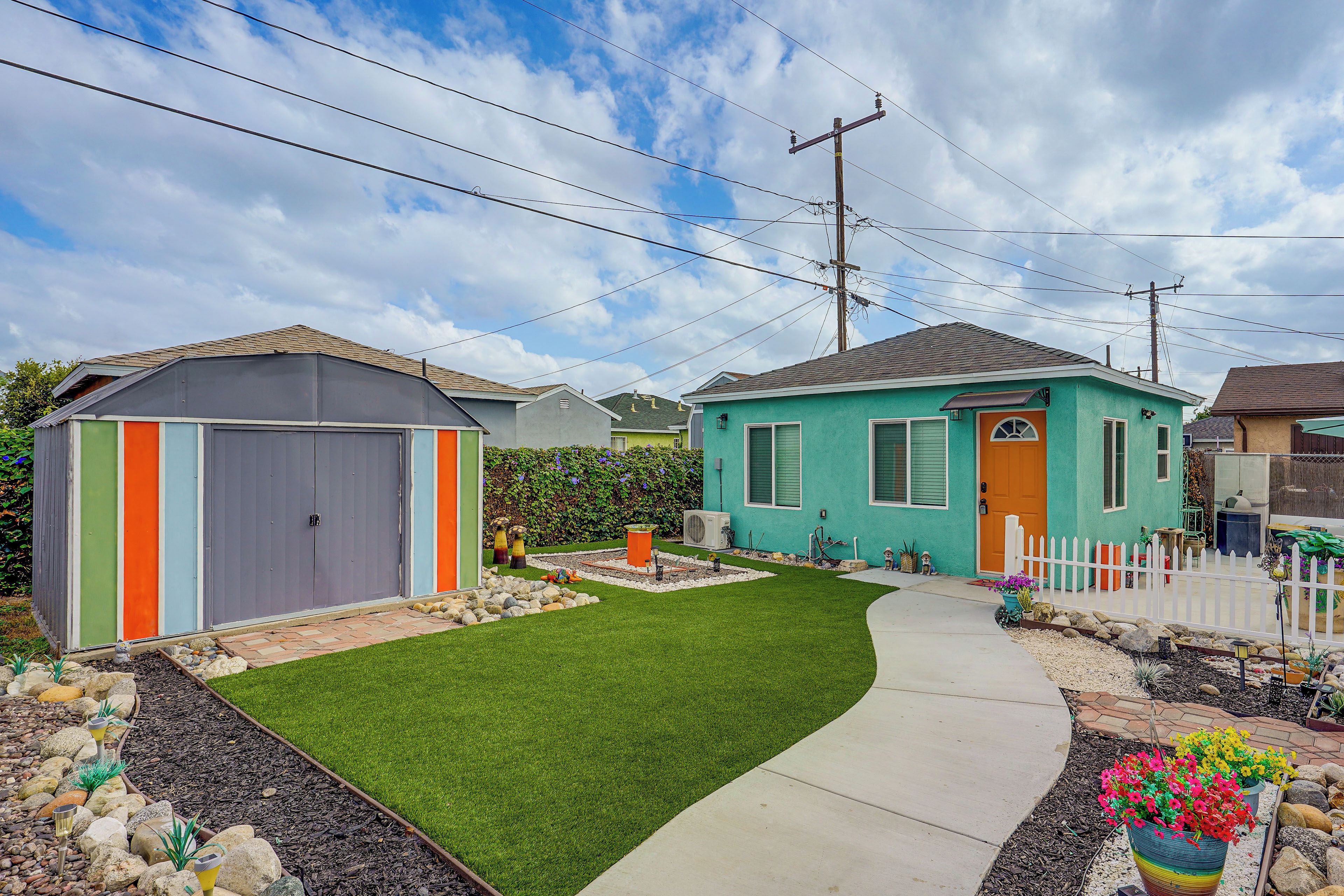 A residential area with a green house, a grey shed, and a well-maintained lawn.