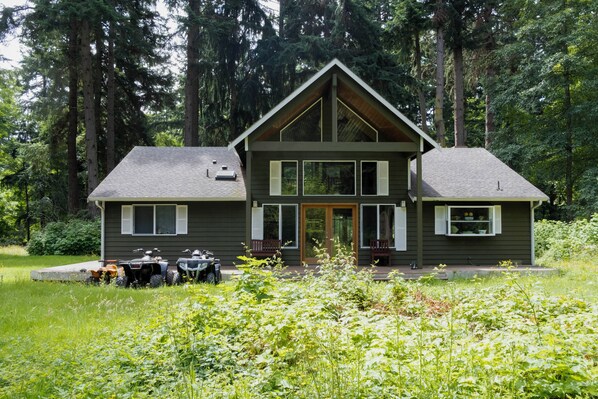 Eine zweigeschossige Holzhütte mit Satteldach, großen Fenstern und einer Veranda mit einer Bank.