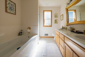 Ein Badezimmer mit einer Badewanne, einem Waschbecken und einem Waschtisch mit Spiegel. Fenster sorgen für natürliches Licht.