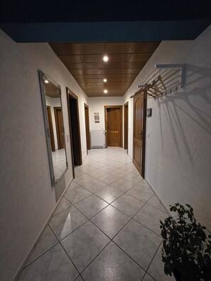 Un couloir doté d’un sol carrelé, de portes en bois et d’un portant à vêtements suspendu.