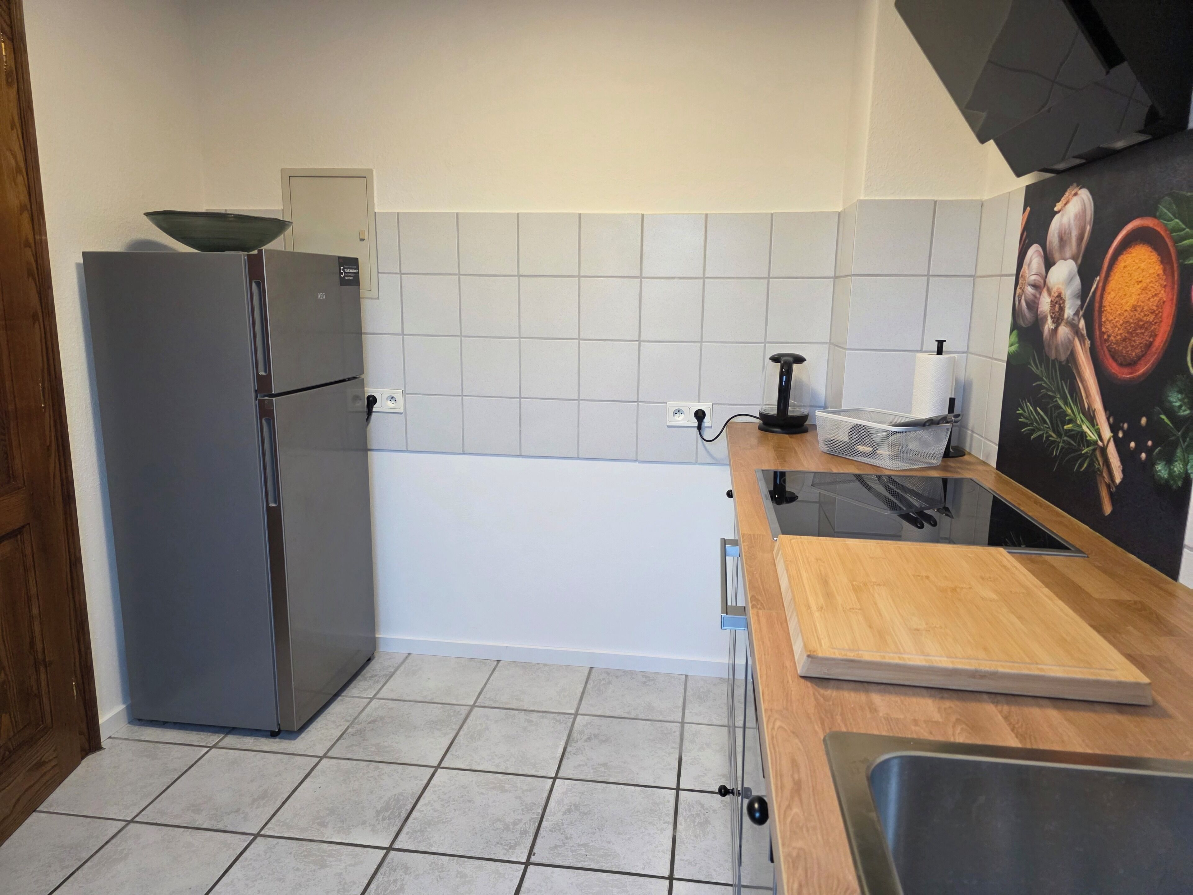 Een keuken met een koelkast, een spoelbak, een houten aanrechtblad en een betegelde achterwand.