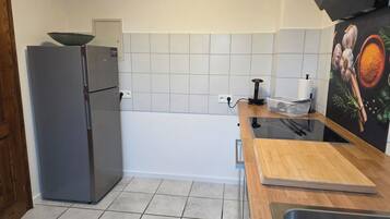 Een keuken met een koelkast, een spoelbak, een houten aanrechtblad en een betegelde achterwand.